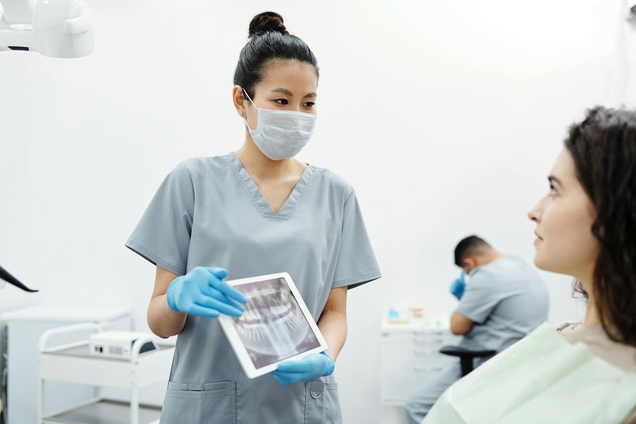 Dentist in scrubs showing dental x-ray on tablet to patient in clinic.